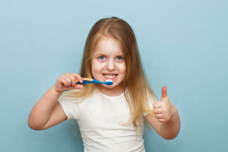 little happy girl brushing her teeth with a toothbrush and smiling on a blue background. thumb upの写真素材