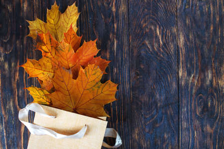 Flat lay creative autumn composition. Gift bag with golden autumn leaves on dark wooden background top view copy space. Fall concept. Autumn background. Minimal concept ideaの写真素材