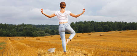 barefoot girl with straw hat stands on a haystack on a bale in the agricultural field after harvesting. bannerの写真素材