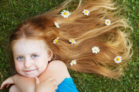 portrait of a beautiful little girl with healthy red hair with chamomile flowers lying on the grass.の写真素材