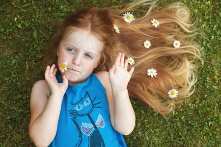 portrait of a beautiful little girl with healthy red hair with chamomile flowers lying on the grass.の写真素材