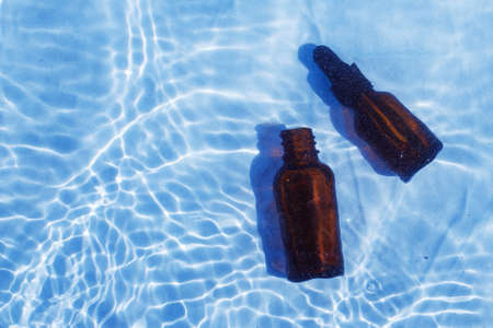 Brown glass oil bottle under fresh water on a blue background. Aromatherapy and perfumes concept.の写真素材