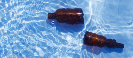Brown glass oil bottle under fresh water on a blue background. Aromatherapy and perfumes concept. bannerの写真素材