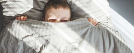 boy sleep in the bed. the child lies on a pillow and covers his face with a blanket. bannerの写真素材