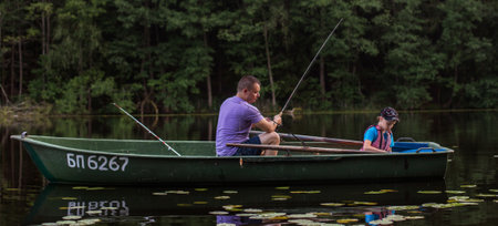 Father and son fishing on rural lake at sunset on a boat. bannerの写真素材