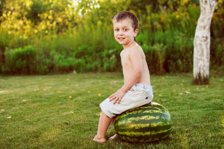 portrait of a happy child boy with a large whole watermelon in the back yardの写真素材