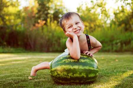 portrait of a happy child boy with a large whole watermelon in the back yardの写真素材