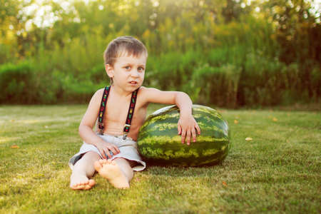 portrait of a happy child boy with a large whole watermelon in the back yardの写真素材