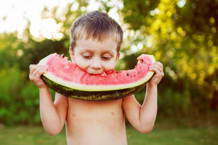 happy smiling child boy eating watermelon outdoor in the backyardの写真素材
