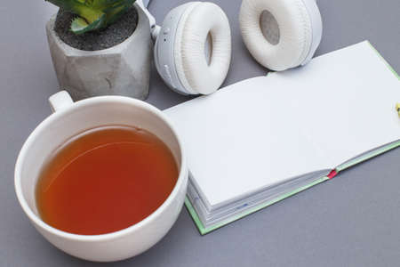 Workplace with a notepad, headphones, a cup of tea or coffee and green plant. Freelancer working space on gray background. Top view.の写真素材