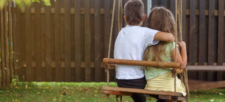children sitting on a swing in the garden. older brother hugging little sisterの写真素材