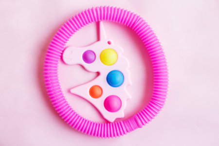 Simple dimple in the form of unicorn and a tube fidget toy on a pink background.の写真素材