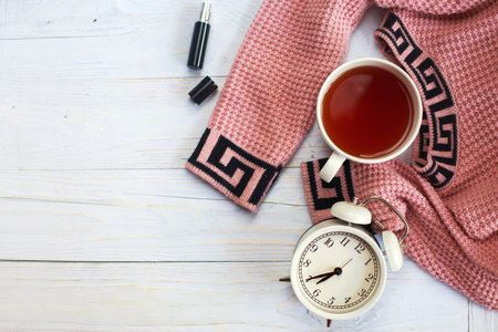 A cup of hot tea, knitted sweater, alarm clock and perfume on a wooden light table. winter morning conceptの写真素材