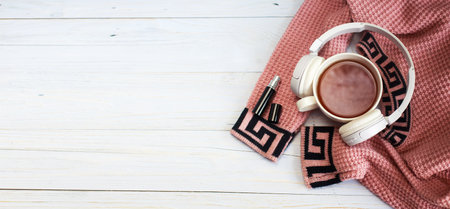 Cozy winter morning at home. Hot tea or coffee, knitted sweater, perfume and headphones on wooden background. Lifestyle and music concept. bannerの写真素材