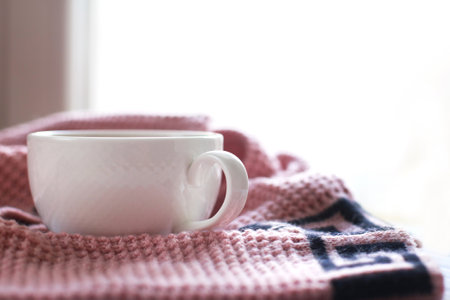 Cup of hot coffee with knitted sweater on a wooden table near the window, winter morning conceptの写真素材