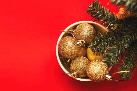 Gold balls and toys in a white cup with a branch of a Christmas tree on a red background.の写真素材