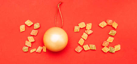 Numeral 2022 from multicolored sweets and golden christmas ball on red background.の写真素材