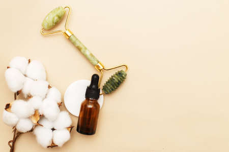 Massage quartz roller for the face of natural nephritis with serum oil in brown glass bottle with a flower of cotton on beige background.の写真素材