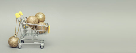 shopping trolley with shiny gold christmas toys balls on a gray background. bannerの写真素材