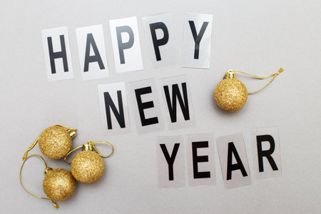 The inscription happy new year with shiny golden Christmas toy balls on a gray background.の写真素材