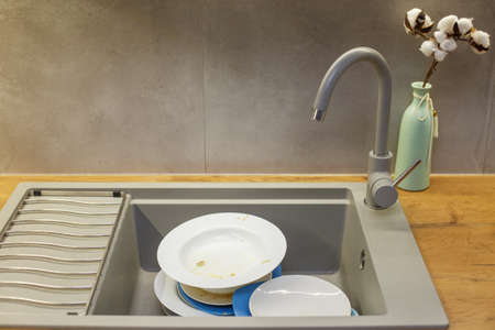 Pile of dirty dishes like plates in the grey modern granite sink in the kitchen.の写真素材