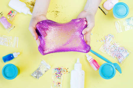 Making slime at home. child holding and stretching colorful slime. DIY concept.Kids hands make purple slime with sequins on a yellow background. Flat lay, top view.の写真素材
