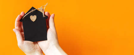 womans hand holding little toy house on an orange background. Home insurance concept.の写真素材