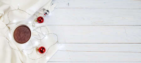 Cup of tea or coffee, knitted white blanket, garland and Christmas decoration balls on light wooden background. christmas morning concept. bannerの写真素材