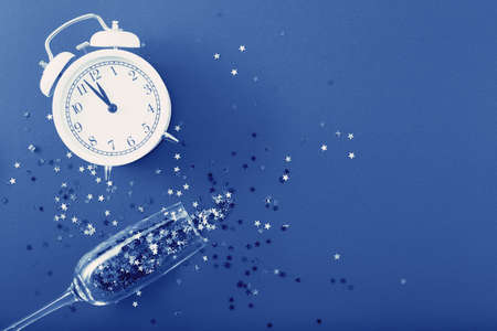 glass with sequins, alarm clock and star shaped confettie on blue backgroundの写真素材