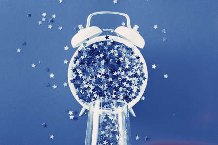 glass with sequins, alarm clock and star shaped confettie on blue backgroundの写真素材