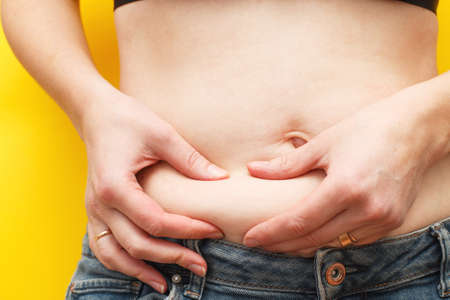 Woman hands compresses the fat on her belly on a yellow backgroundの写真素材