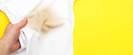 female hand holding white clothes with a dirty stain on a yellow background. bannerの写真素材