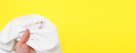 Woman holding a white shirt with red kiss lipstick on a yellow background. concept of treason and infidelityの写真素材