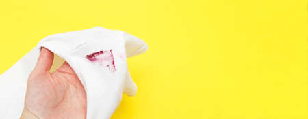 female hand holding white shirt with red lipstick stain on yellow background. bannerの写真素材