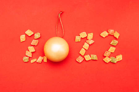 Numeral 2022 from multicolored sweets and golden christmas ball on red background.の写真素材