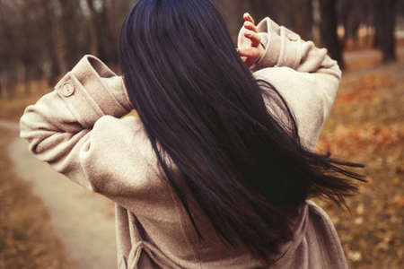 portrait of brunette hair woman in beige coat walking at the city parkの写真素材