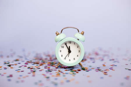 Alarm clock showing five minutes to twelve on a purple background with milticolored sequins.の写真素材