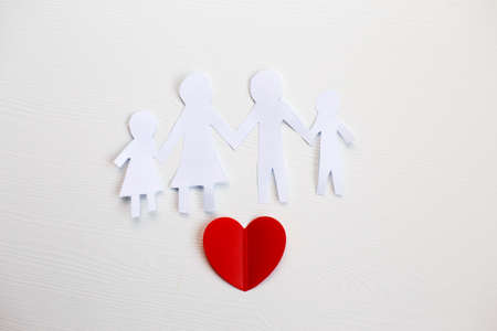 Happy paper cut family holding hands on a light wooden background with red heartの写真素材