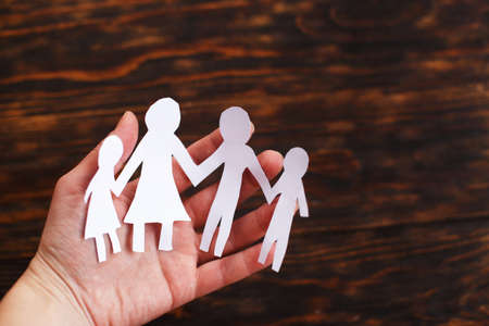 human hand holding happy paper cut family on a brown wooden background.の写真素材
