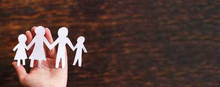 human hand holding happy paper cut family on a brown wooden backgroundの写真素材