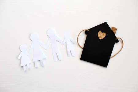 Happy paper cut family holding hands on wooden background near little toy house.の写真素材