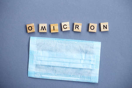 word omicron made by wooden blocks with medical mask on gray backgroundの写真素材