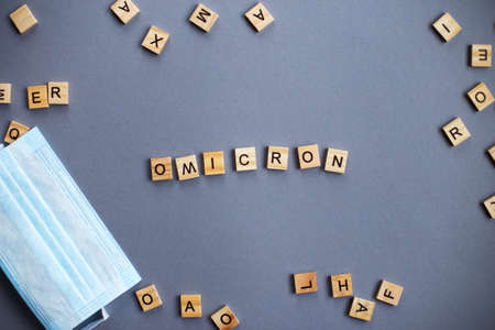 word omicron made by wooden blocks with medical mask on gray backgroundの写真素材