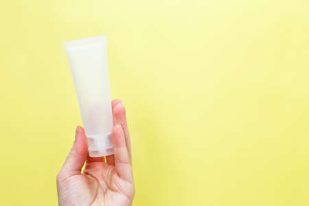 Female hand holding cream tube cosmetic products on a yellow background.の写真素材