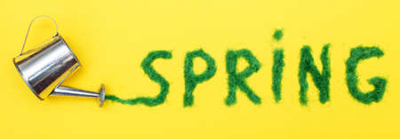 The inscription Spring from a decorative green grass on a yellow background with a watering can. bannerの写真素材