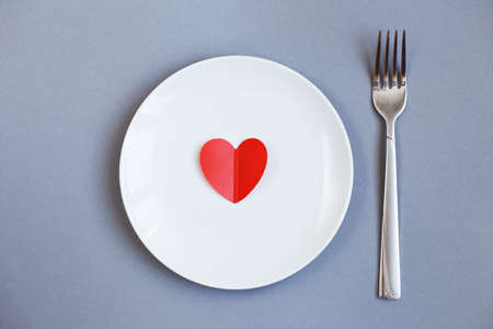 Red Heart on a white plate with fork on gray background.の写真素材