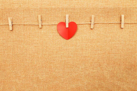 red heart on clothes pin on brown textile background.の写真素材