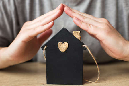 woman's hand covered little toy house. home insurance concept.の写真素材