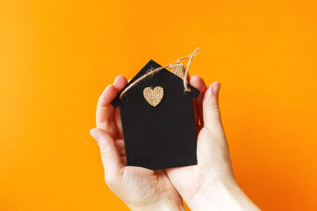 woman's hand holding little toy house on an orange background. home insurance concept.の写真素材