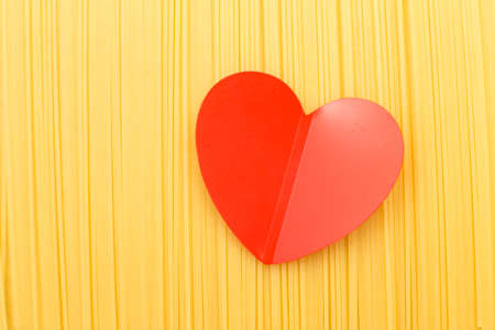 spaghetti yellow background with a red heart close. raw pasta macroの写真素材